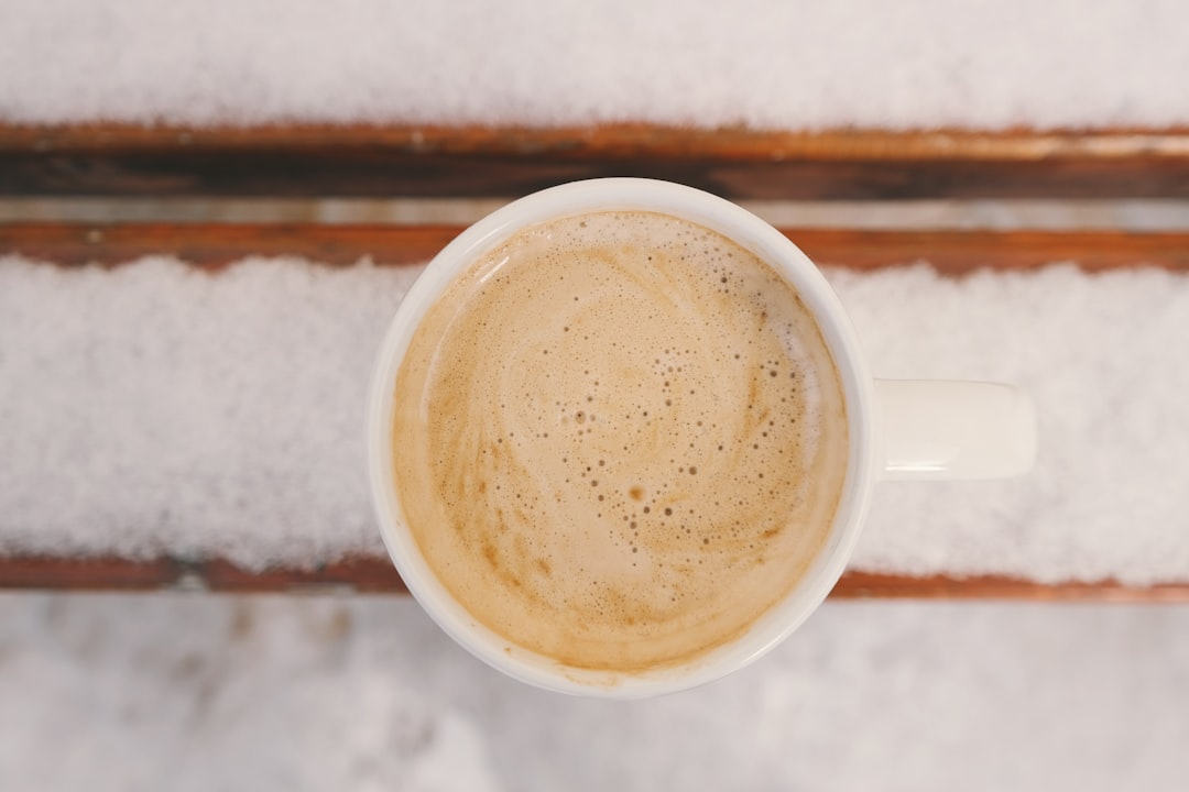 A hot coffee drink held near a cafe window on a snowy day. Hot coffee drink in a paper cup held near a cafe window with snow visible outside