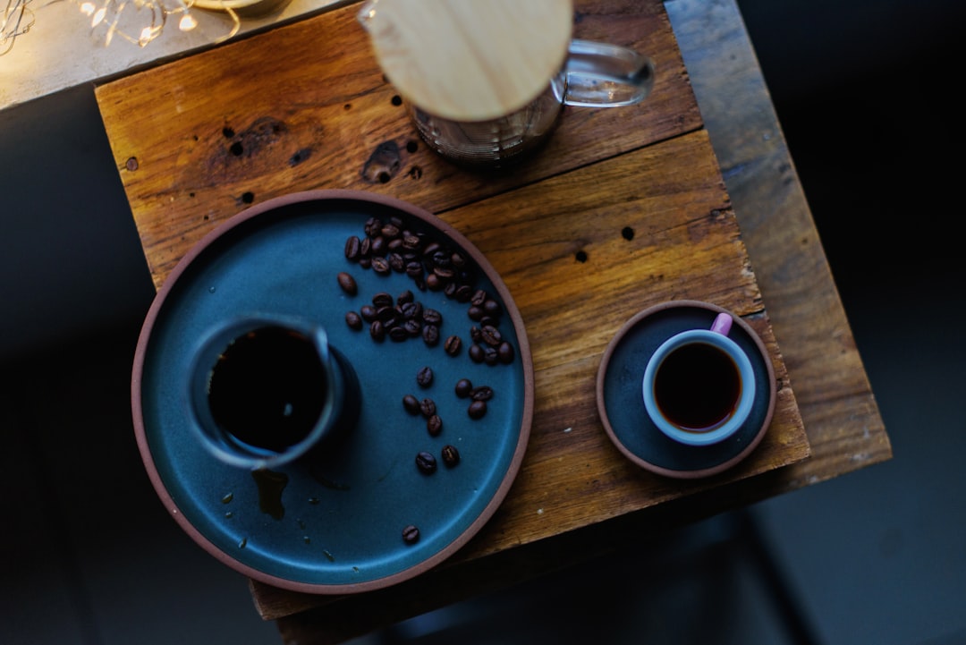 Coffee beans and a simple tasting setup on a wooden table. Coffee beans in a bowl on a wooden table with a cup of black coffee beside it